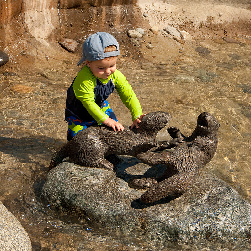 Young boy playing on a bronze otter sculpture at the East Bay Public Plaza, Olympia WA
